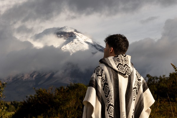 Hombre con un poncho tradicional ecuatoriano de espaldas, mirando el imponente Volcán Cotopaxi en Ecuador.