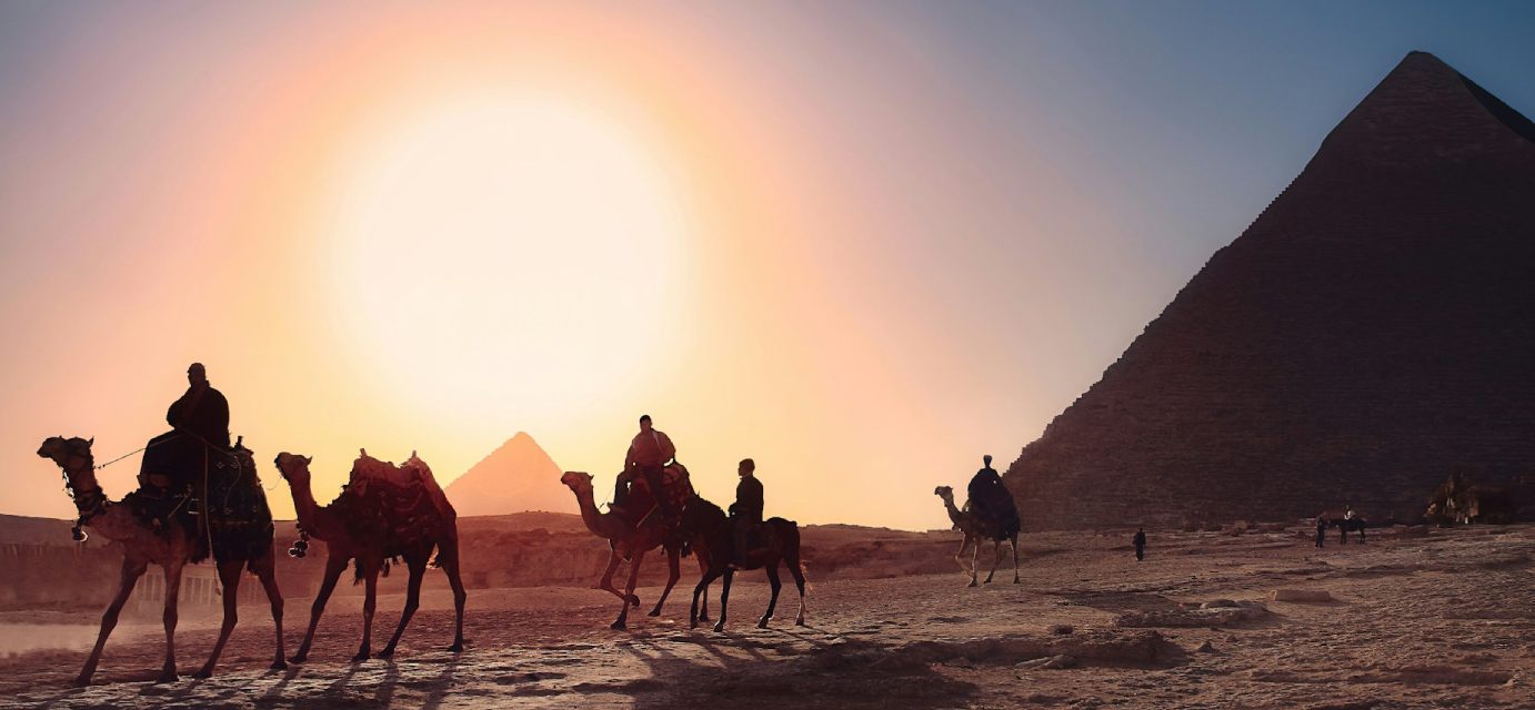 imagem de uma das cidades do Egito, com um homem em primeiro plano e uma das pirâmides ao fundo, em artigo de blog sobre viagem para o Egito