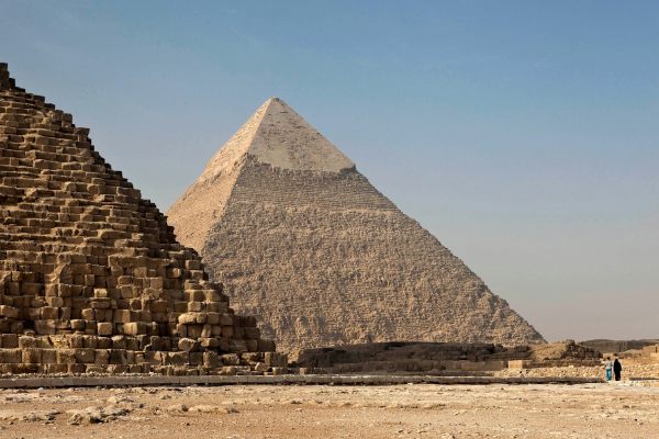 imagem de pessoas andando com camelos no Egito, com uma das pirâmides ao fundo, em artigo de blog sobre viagem para o Egito