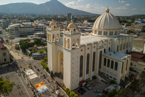 Vistas aéreas de la Catedral Metropolitana en la plaza principal del centro histórico de San Salvador, capital de El Salvador, con montañas y volcanes en el fondo.