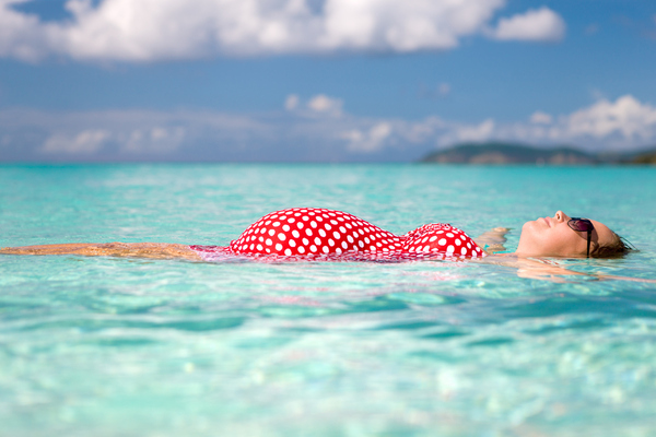 Mujer embarazada flotando en el agua en la playa del caribe