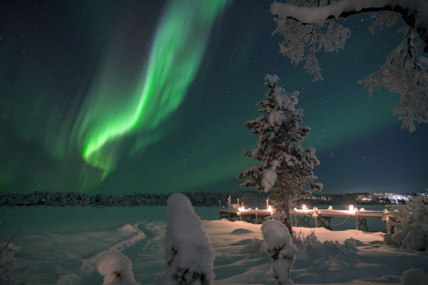 Aurora boreal y árboles nevados cerca de un muelle en Kiruna, Suecia.