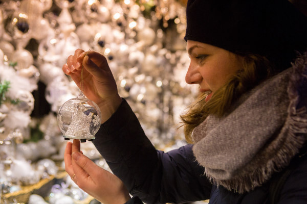 Mujer abrigada sosteniendo adorno navideño en una tienda con una sonrisa.