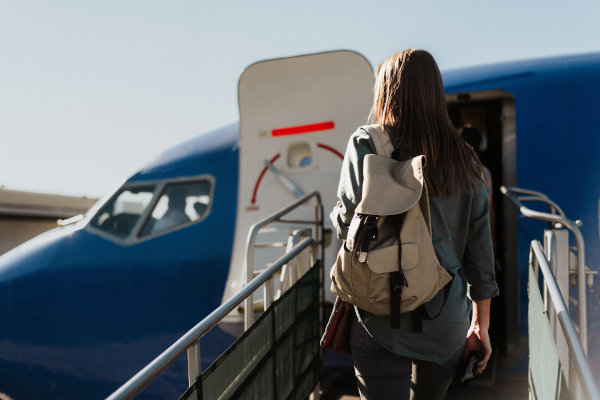 Pasajera con mochila gris colgada en un hombro a punto de entrar en el avión en el aeropuerto.