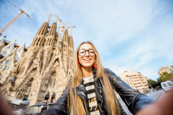 Turista sonriente sacándose una selfie frente a la Sagrada Familia en Barcelona.