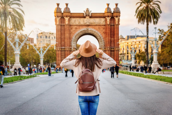 Mujer turista con mochila y sombrero admirando el famoso Arco del Triunfo en Barcelona, España.
