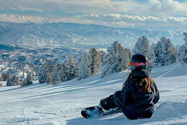 una mujer sentada sobre la nieve con su tabla de snowboard observando el paisaje