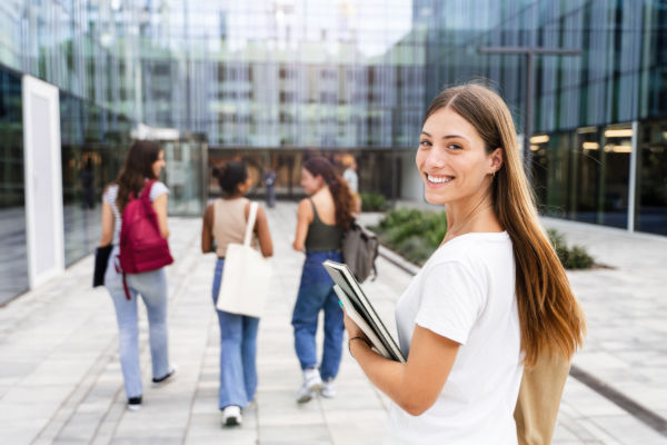 Joven estudiante entrando a su universidad, con libros y cuadernos en su mano.