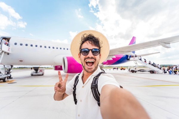 Turista masculino feliz tomándose una selfie a punto de embarcar en un avión en el aeropuerto
