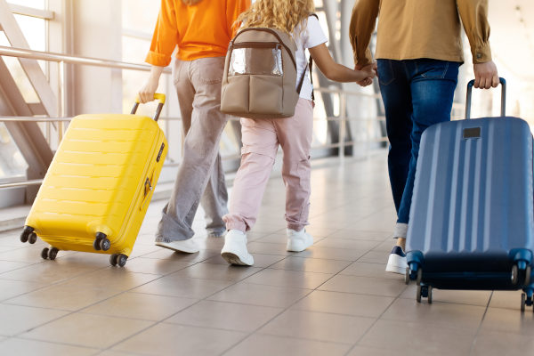 Primer plano de la familia caminando juntos en el aeropuerto tomados de la mano y llevando valijas con ruedas.