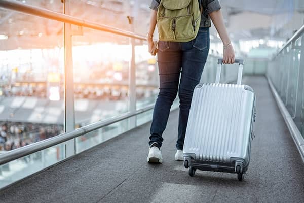 Mulher de costas andando em direção ao avião puxando sua mala de viagem.