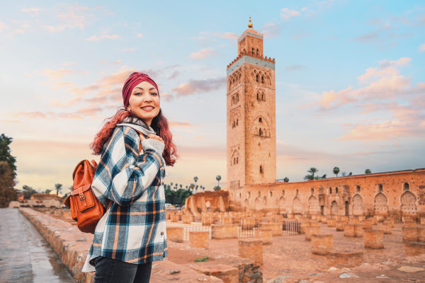 Mujer turista con mochila posando junto a la mezquita de Koutoubia en Marrakech, Marruecos, a la hora del atardecer.