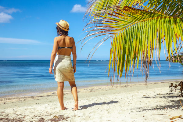 Mujer de espaldas caminando por las arenas blancas de West Bay Beach, Roatán, Honduras, con vistas al mar azul en un día soleado.