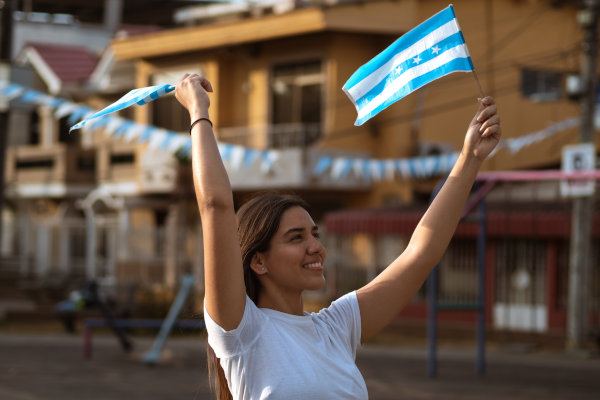 Chica joven ecuatoriana sonriendo mientras agita en el aire la bandera de Guayaquil en una celebración.