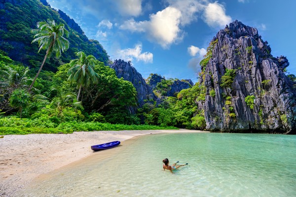 Mujer echada en las orillas del mar cristalino en Hidden Beach en la isla Matinloc, El Nido, Palawan, Filipinas, con formaciones rocosas y vegetación de fondo.