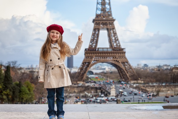 Niña rubia con boina y abrigo señalando la torre Eiffel en un día nublado en París