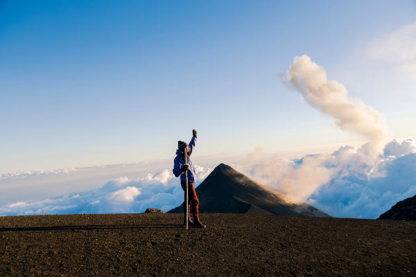 Alpinista celebrando en la cima del volcán Acatenango en Guatemala con el Volcán de Fuego en el fondo.