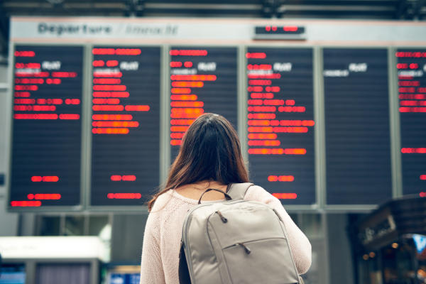 Mujer de espaldas con mochila viendo la pantalla que indica las partidas y llegadas en un aeropuerto.
