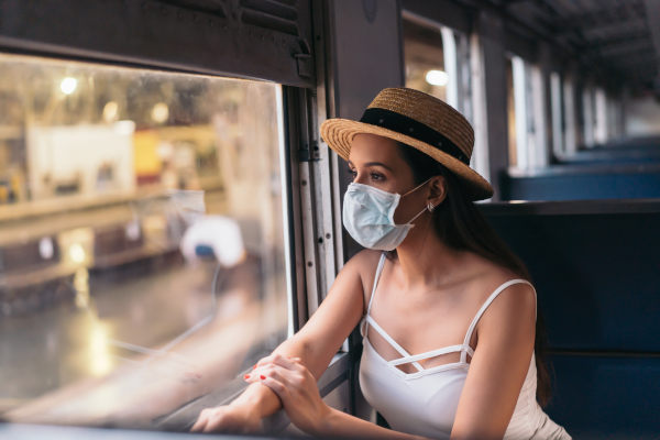 Mujer viajando en tren en el extranjero con mascarilla puesta mientras mira por la ventana.