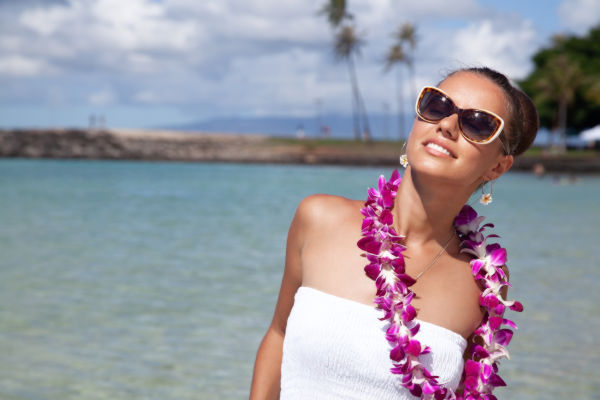 Turista con gafas de sol y collar de flores disfrutando del sol en una playa de Hawaii, con el mar de fondo.