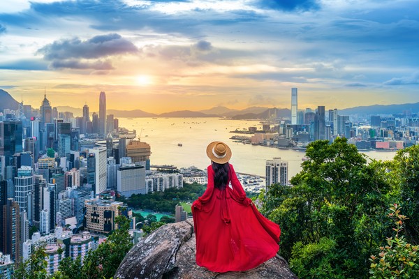 Turista mujer con vestido rojo en el mirador de Hong Kong al atardecer.