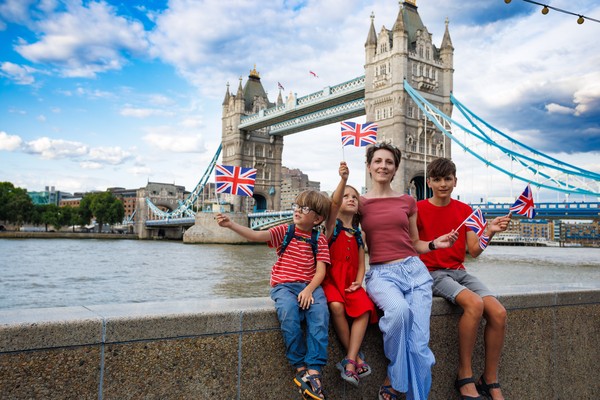 Familia sentada en una barandilla a orillas del río Támesis con el Tower Bridge de fondo.