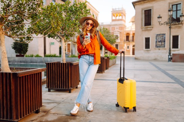 Turista con maleta amarilla en una plaza usando el celular.