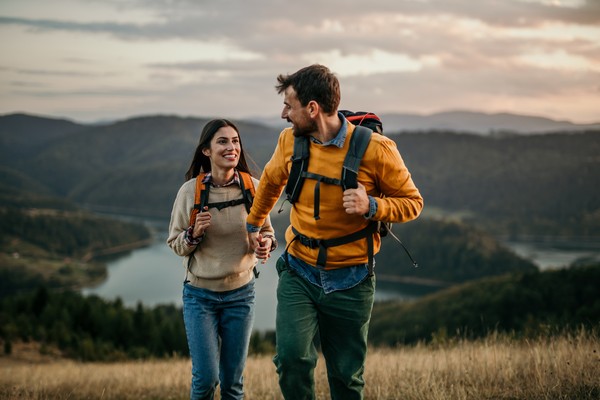 Foto de una pareja de senderistas caminando por la montaña con lago en el fondo.