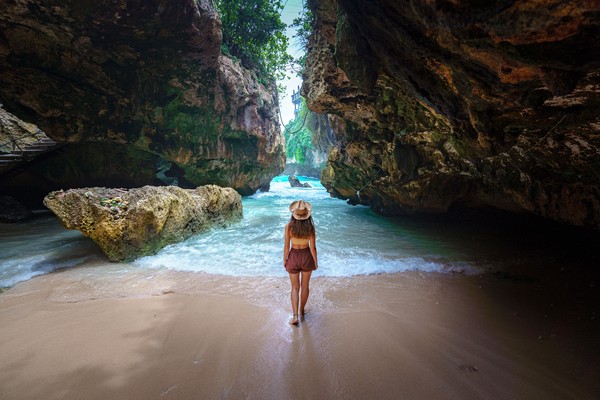 Parte posterior de la mujer viajera con sombrero en la playa entre las rocas en la isla de Bali.