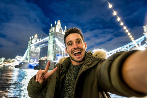 Hombre turista feliz tomándose una selfie junto al Tower Bridge de Londres por la noche.