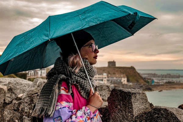 Mujer de paseo por Irlanda con paraguas y abrigada mirando hacia el cielo nublado.