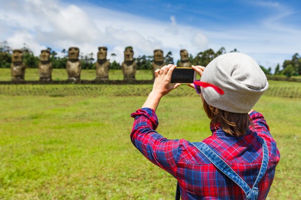 Mujer turista tomando fotografía de los moáis en un día soleado en Isla de Pascua, Chile.