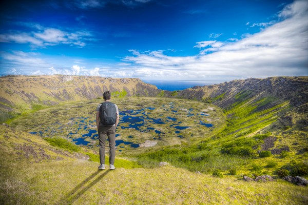 Hombre con mochila parado con las manos en los bolsillos en el borde del cráter del volcán Rano Kau, Isla de Pascua, Chile.