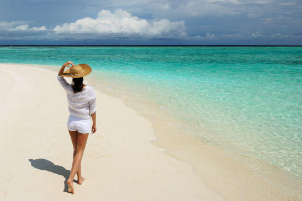Mujer con sombrero de sol en playa tropical de arena blanca y aguas turquesas.