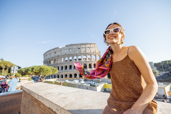 Mujer turista en Roma posando para una foto sentada en una barandilla con el Coliseo Romano de fondo en un día soleado