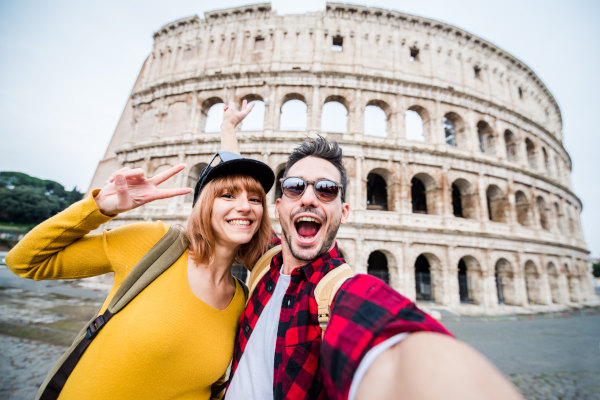 Pareja sonriente sacándose una selfie junto al Coliseo Romano en un día nublado.
