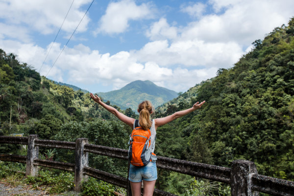 Mujer turista contra la barandilla de un sendero abriendo los brazos con vistas hacia la exuberante vegetación de las Blue Mountains en Jamaica.
