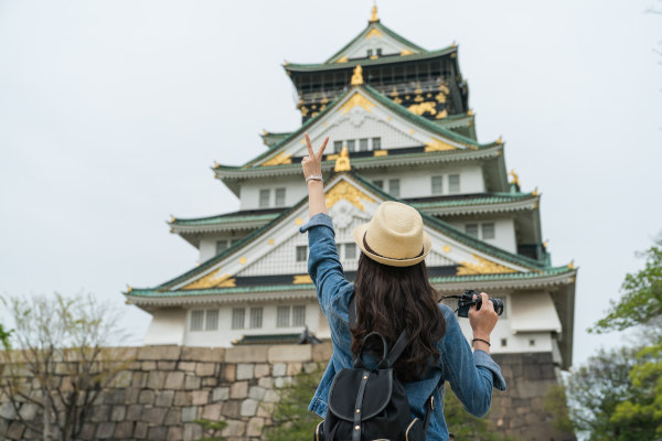 Mujer viajera tomando fotografía del magnífico castillo de Osaka con gesto de la mano de victoria.