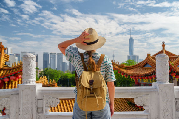 Turista con mochila y sombrero observando el skyline de Kuala Lumpur desde el templo Thean Hou, con arquitectura tradicional en primer plano.