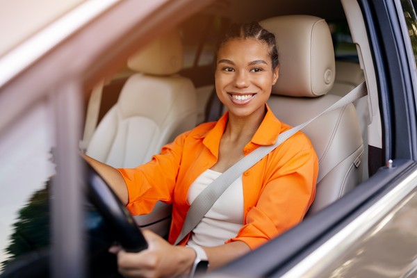 Mujer sonriente conduciendo auto con cinturón de seguridad puesto.