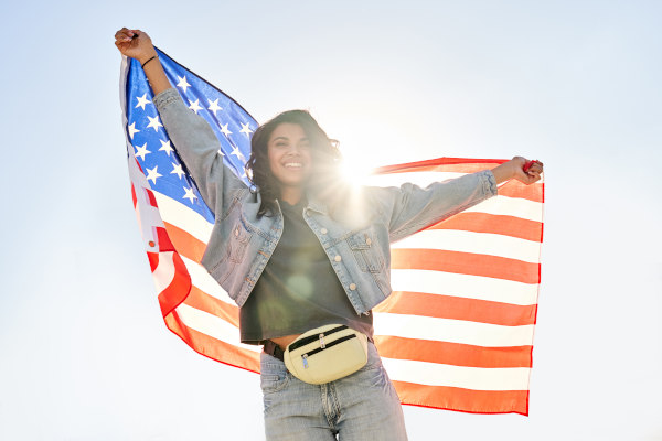 Mujer afrodescendiente con los brazos extendidos, sosteniendo la bandera de Estados Unidos a contraluz