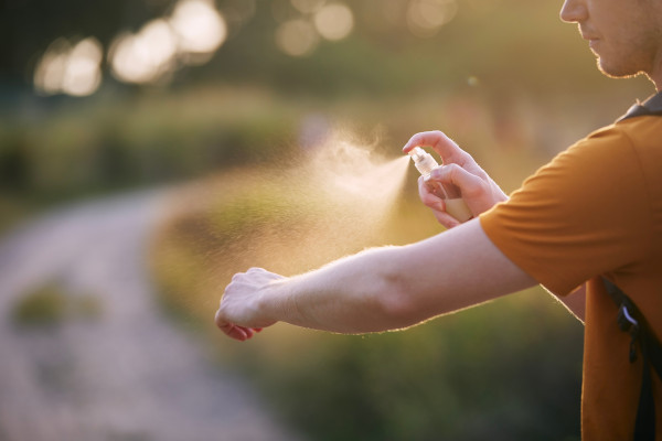 Hombre aplicándose repelente contra insectos en spray al aire libre.