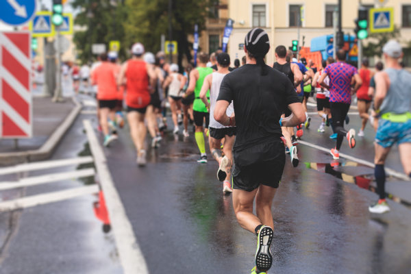 Multitud de corredores de maratón urbano cerca de semáforos con calzada húmeda de lluvia reciente.