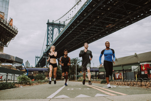 Cuatro corredores de distintas etnias corriendo por las calles de la ciudad de Nueva York.