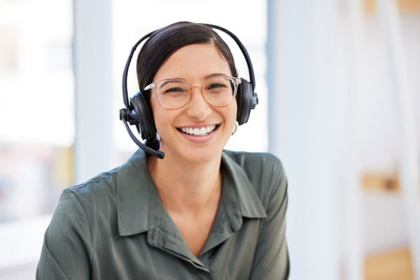 Personal femenino de atención al cliente con gafas, auriculares y micrófono sonriendo a cámara.