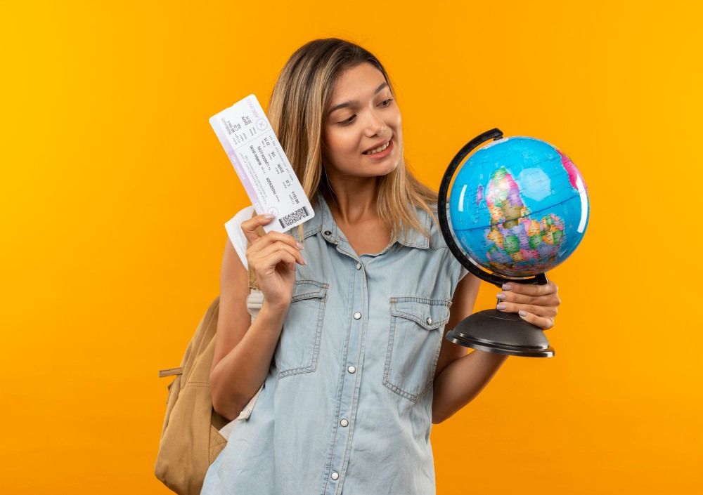 Mulher de chapéu com roupa vermelha, debruçada em uma mala vermelha, com uma passagem aérea na mão, para ilustrar um artigo de blog sobre seguro viagem cartão de crédito