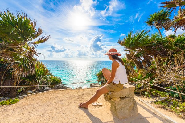 Mujer sentada en un banco de piedra contemplando el mar turquesa en Tulum, Riviera Maya, México