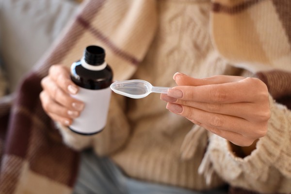 Mujer con una botella de jarabe para la tos y cucharilla lista para tomarlo.