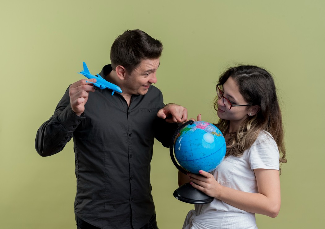 Casal composto por homem e mulher segurando nas mãos um globo terrestre e um avião de brinquedo, representando a busca pelo melhor seguro viagem internacional 2025