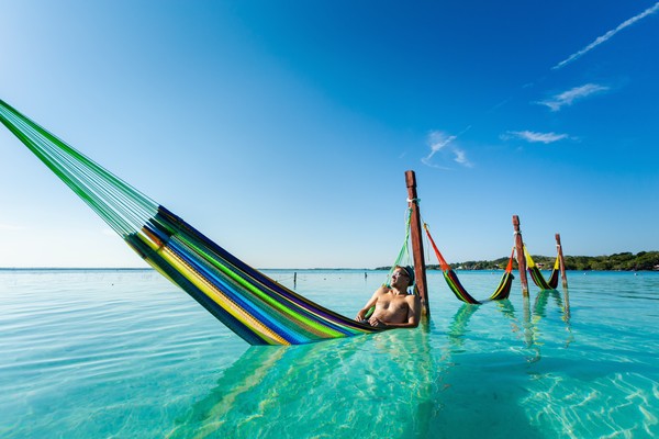 Turista masculino relajándose en una hamaca en la Laguna Bacalar en México.